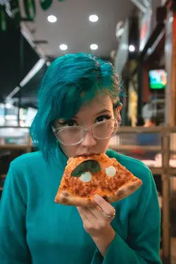 a young girl with green hair color and green shirt is eating a slice of pizza