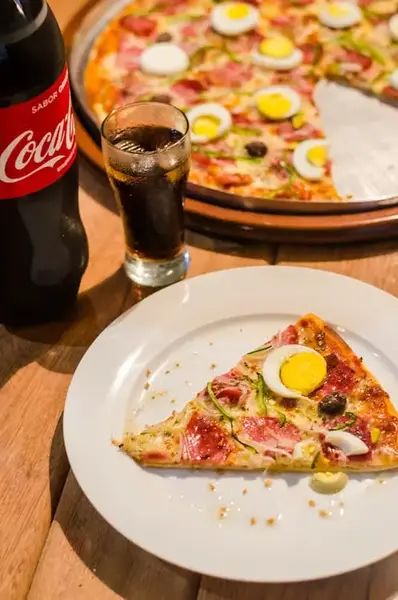 a slice of pizza contain a half of egg on the white plate near by glass of coca